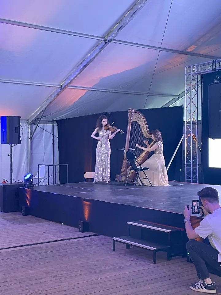 Performance musicale lors de l’événement des 50 ans de l’ACIS, avec une violoniste et une harpiste en tenue de soirée sur scène sous chapiteau, captées par un photographe professionnel