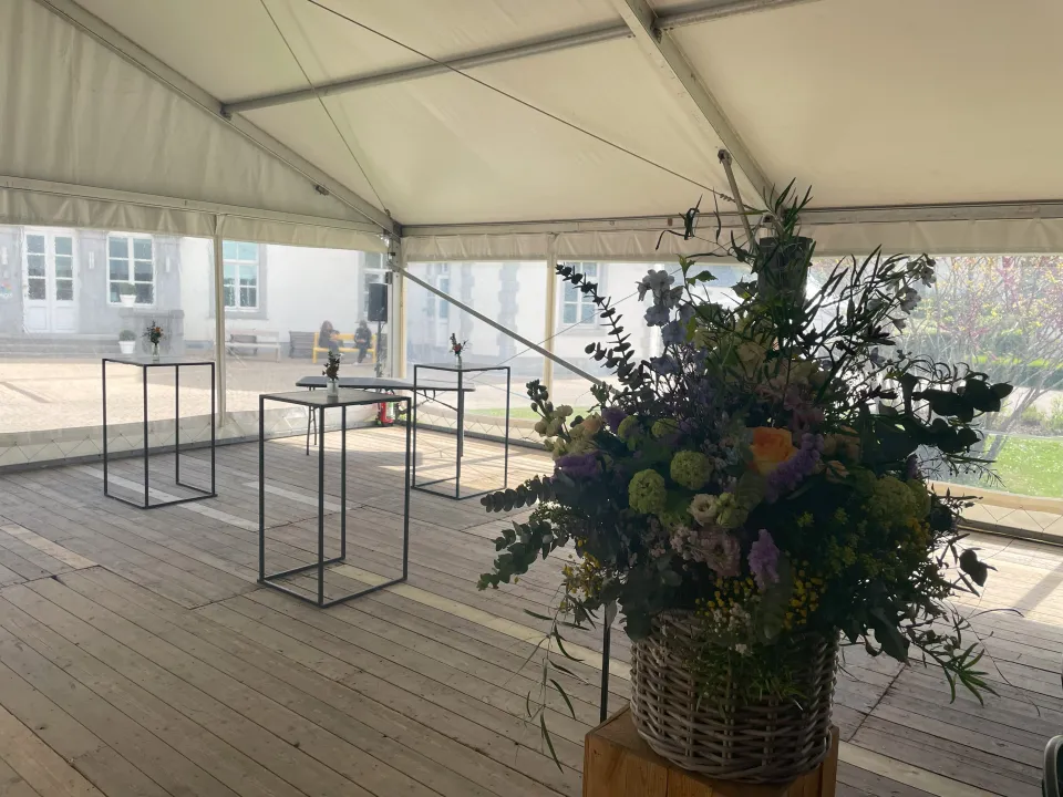 Espace de réception sous chapiteau pour l’événement des 50 ans de l’ACIS, avec plancher en bois, mobilier haut minimaliste et décoration florale soignée en premier plan"