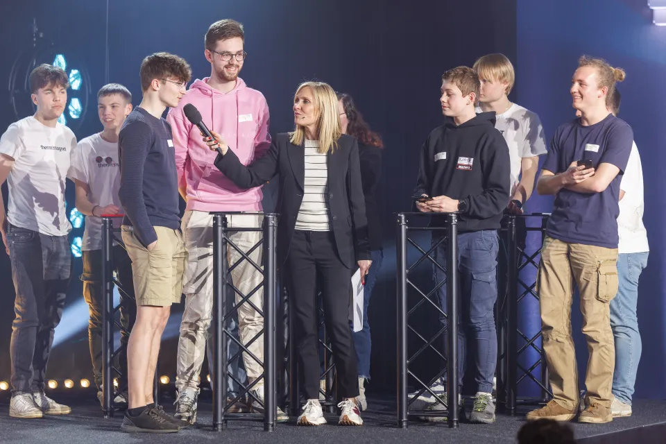 Séquence d’interview sur scène pendant L’Odyssée de l’Objet, où l’animatrice interroge une équipe de jeunes finalistes, répartis en deux groupes, sous des projecteurs lumineux.